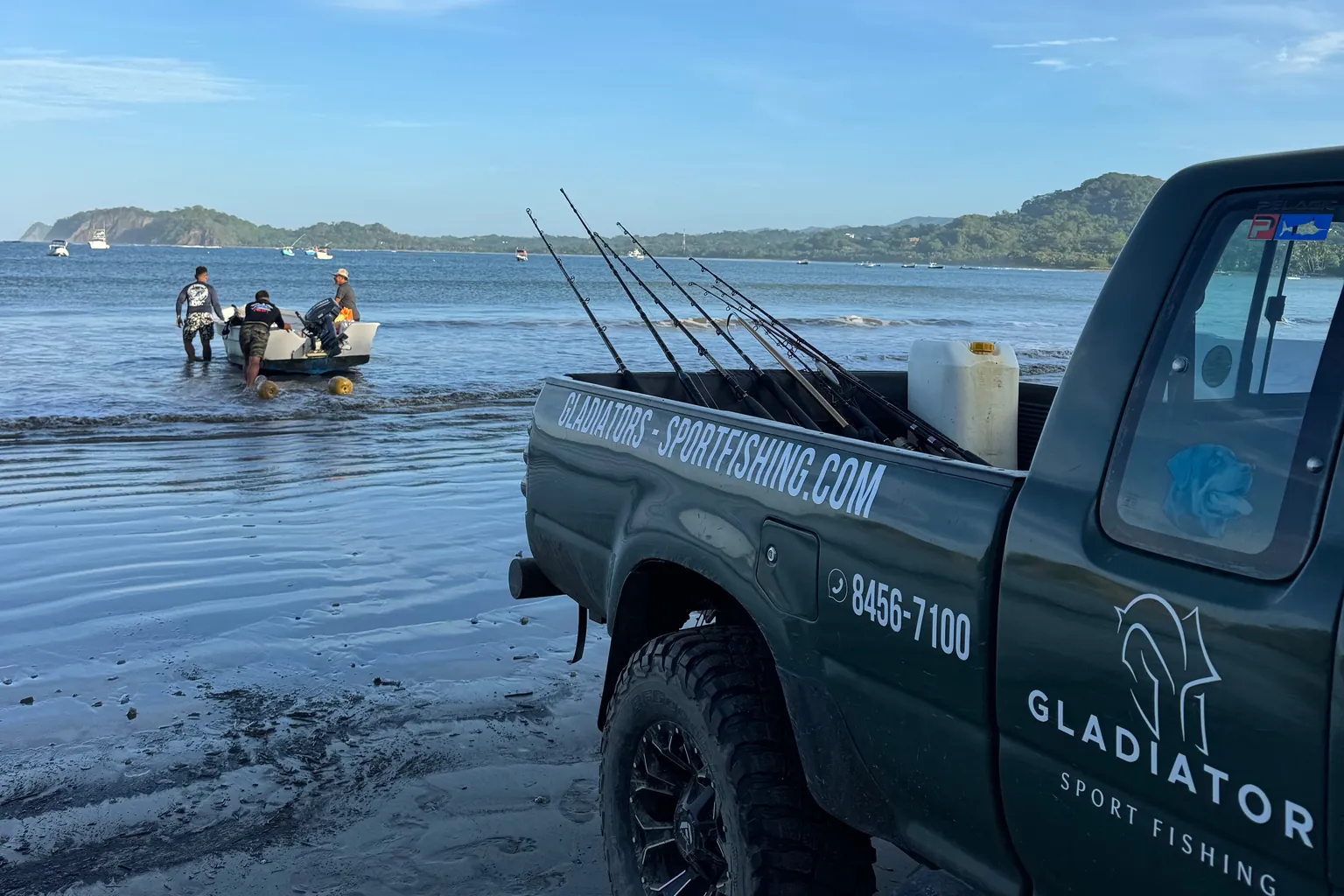 Pick-up Gladiator sulla spiaggia, con persone accanto alla piccola barca nell’acqua bassa